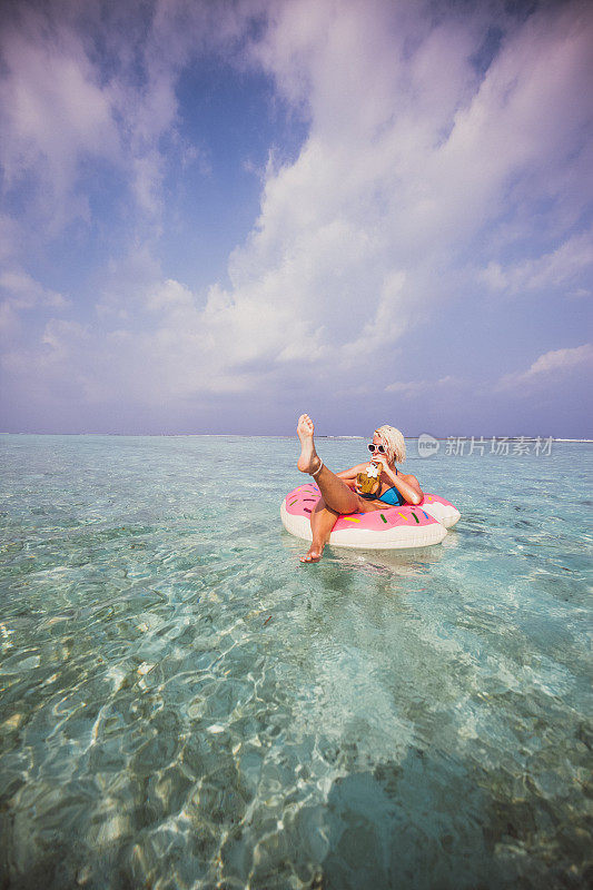 一个金发女人在马尔代夫的海上漂浮在充气甜甜圈上