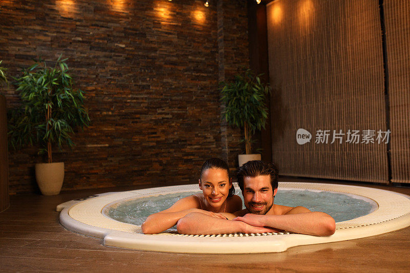 一对美丽的夫妇在健康水疗中心的热水浴缸里放松。