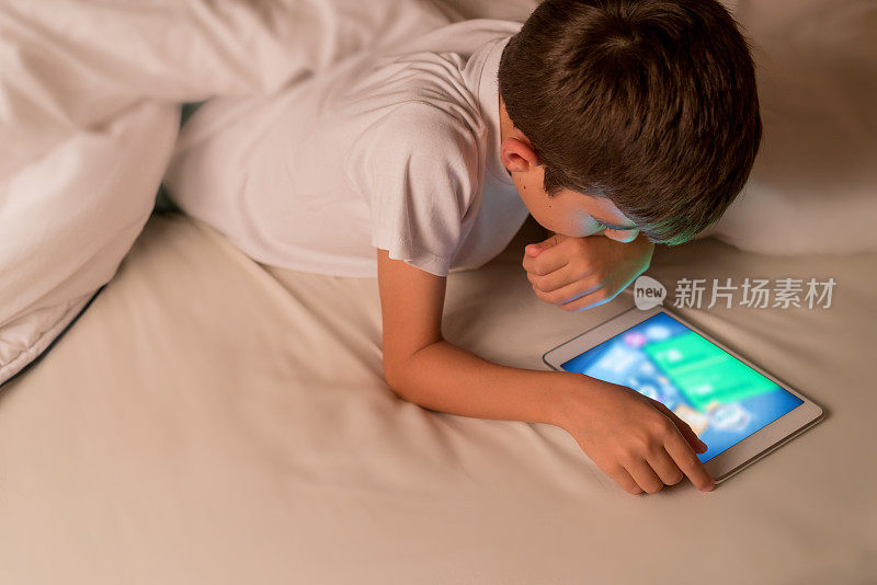 男孩晚上在床上看数字平板电脑