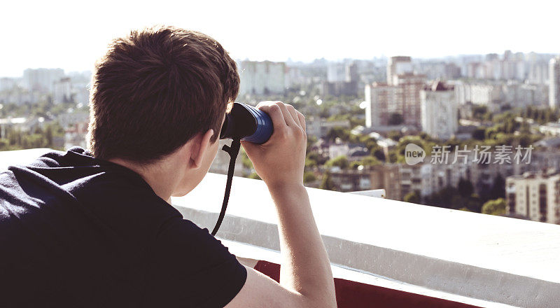 一个年轻人用双筒望远镜从屋顶上看