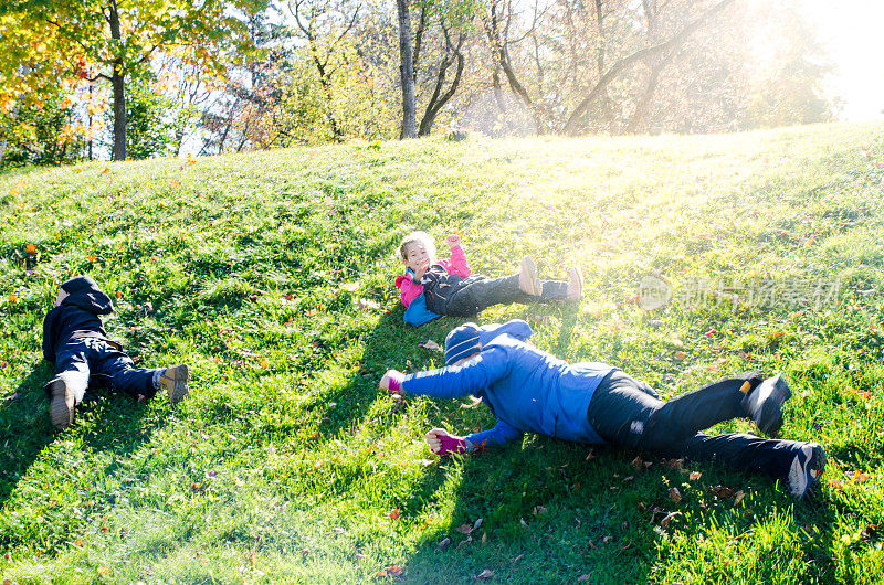 母亲，儿子和女儿在一个公园的草山上滚动在秋天的一天