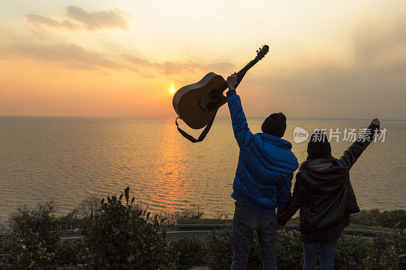 一对年轻夫妇拿着吉他站在山坡上