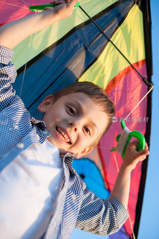 快乐的小男孩把风筝举过头顶，看着镜头