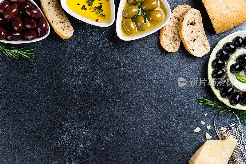 橄榄，夏巴塔面包，奶酪，油，香草和香料在黑色的石头背景。地中海的零食。开胃菜gourman食物。本空间