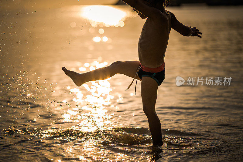 无忧无虑的男孩站在海里用腿泼水。