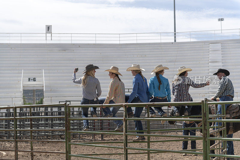 年轻的女牛仔朋友们坐在围栏上自拍