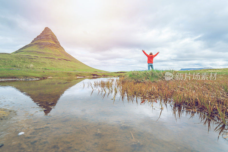 冰岛的年轻女子在著名的Kirkjufell山的春天阴云密布的天空中张开双臂争取自由