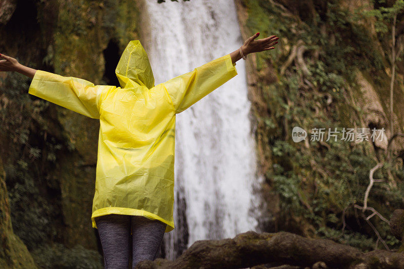 一个穿着黄色雨衣站在瀑布前的女人