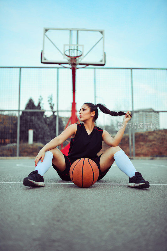 可爱的女运动员坐在篮球场上玩头发