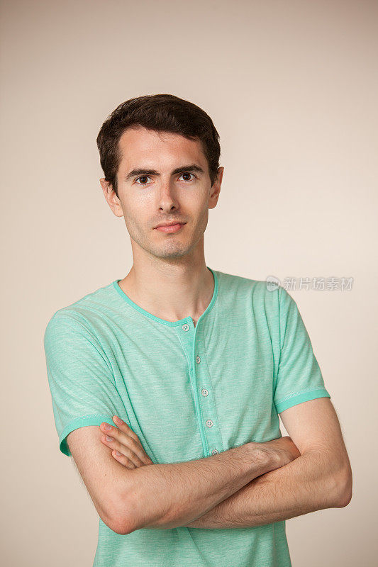 一名30岁男子在米色背景上穿一件绿松石t恤的工作室肖像