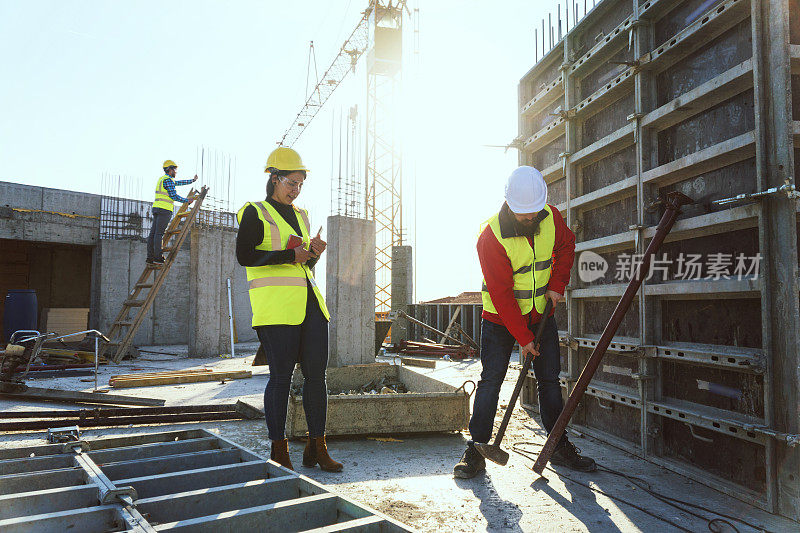 一个阳光明媚的日子，一位自信的女建筑师拿着平板电脑和一位建筑工人在一个住宅楼的工地上一起讨论和工作。