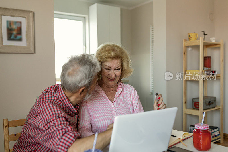 网上购物是最好的购买方式。幸福的老夫妇谈论使用笔记本电脑一起吃早餐，惊讶兴奋的年长妇女看着电脑屏幕上显示微笑的中年丈夫在网上购物在网站上销售