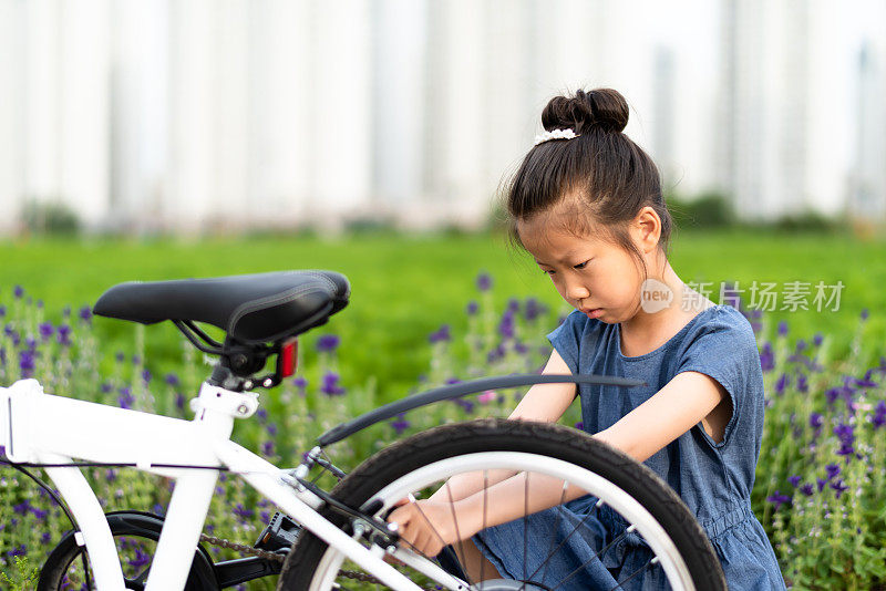 亚洲小女孩在草坪上修理自行车