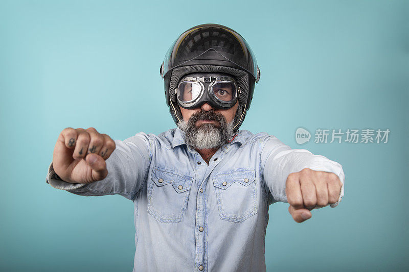中年白种人，蓄着胡子，戴着头盔和眼镜，假装骑摩托车