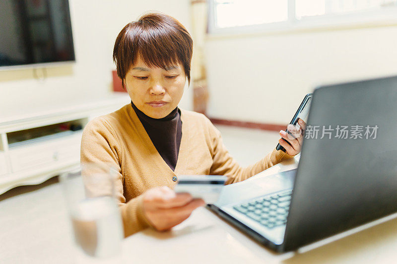 一位中年妇女正在家里用信用卡购物——技术与生活、信用卡、银行与支付的概念