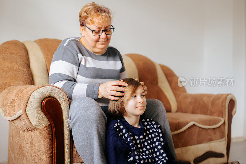 一位年长的妇女和她的孙女一起坐在沙发上，手放在头上