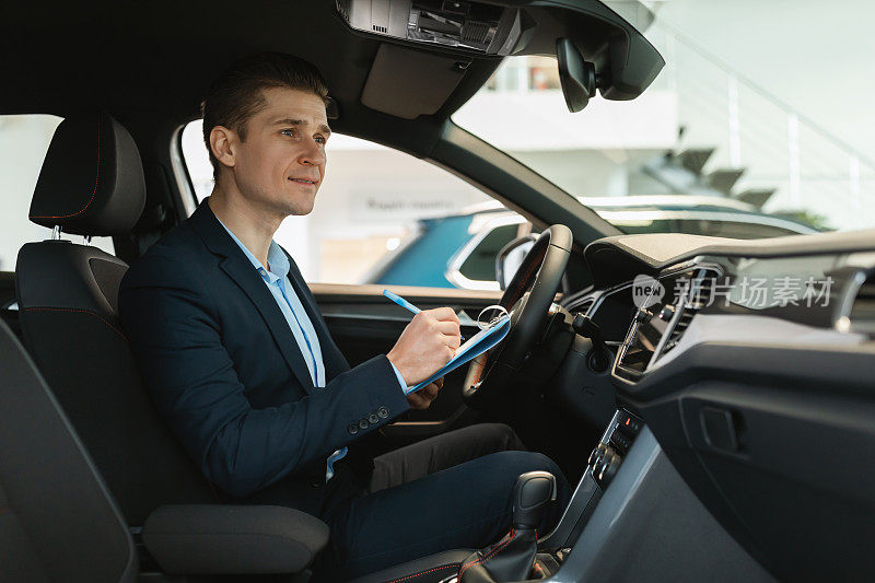 自信的年轻汽车销售员坐在新车里，做检查，在经销商处记录信息，复制空间