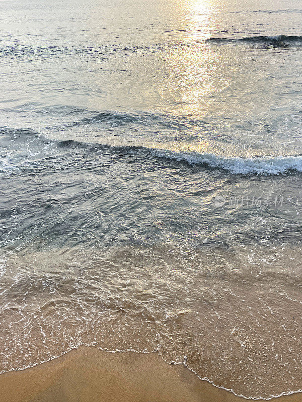 海浪在沙滩上破碎的全画幅图像，潮汐和海洋运动，落日在水面上的反射，水的边缘壁纸背景，高架视图