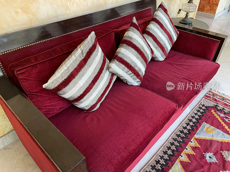 红色天鹅绒软垫沙发的特写图像与三个红，白，灰，条纹方形靠垫，抬高的观点，重点在前景