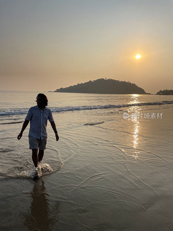 印度果阿的帕洛勒姆，果阿海滩度假的印度人，日落时从海里涌出来的特写照片，度假的游客赤脚走在海滩上，在水里戏水，聚焦在前景