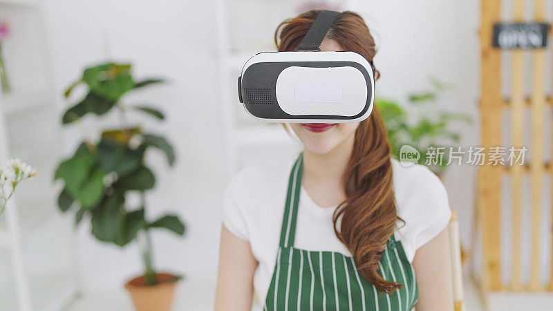 年轻的亚洲女性开花店时戴着VR眼镜工作，通过虚拟现实耳机挑选鲜花。商业和技术理念，虚拟虚拟