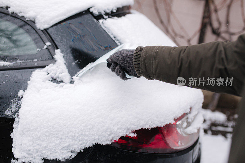 第一人称视角，一个人用刮雪机在车上擦雪窗。关注刮刀。寒冷的雪和霜的早晨。黑色的车
