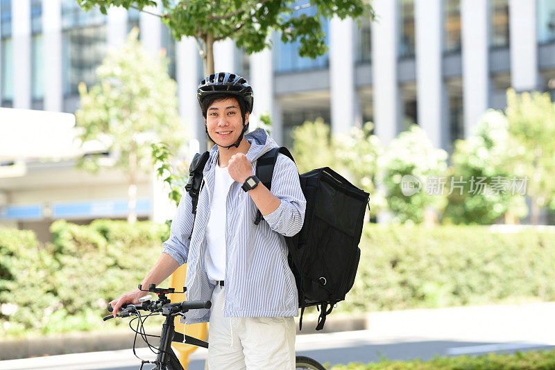 一名年轻的亚洲男子背着双肩包，骑着自行车在送快递