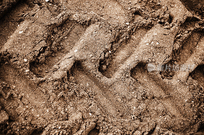 棕色污垢或泥地或砂砾路面的水平照片，带有轮胎标记设计，轮胎胎面或凹槽或图案，浅的大标记形成小凹坑