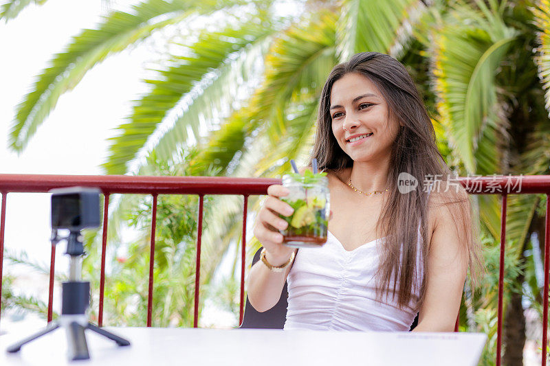一个女人坐在阳台上，面前放着一台照相机。在现代咖啡馆拍摄社交媒体博客