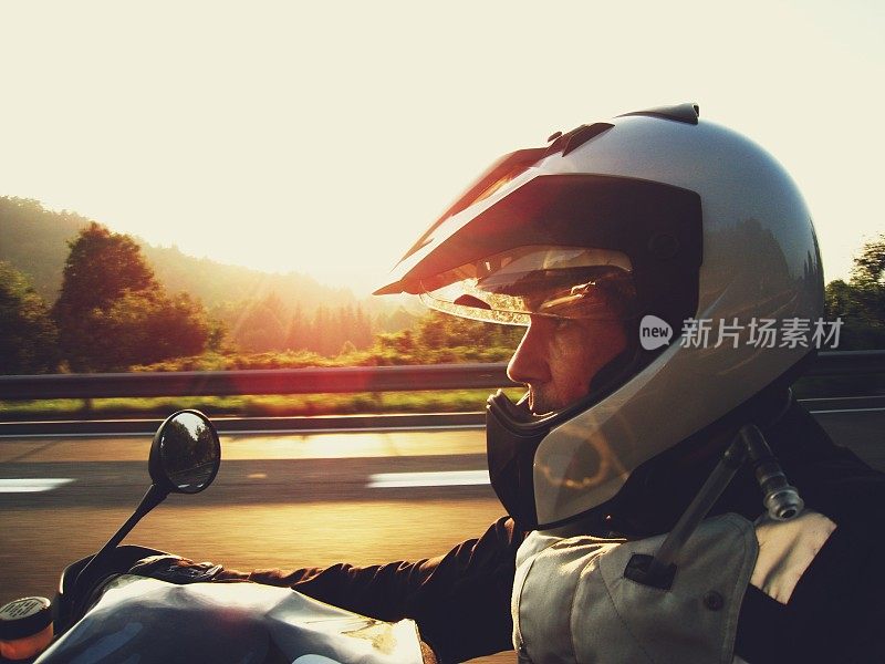 夕阳西下，一名戴着银色头盔的男子骑着摩托车