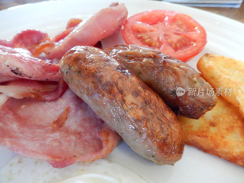 这是一份有香肠、培根、土豆泥和西红柿的油炸早餐