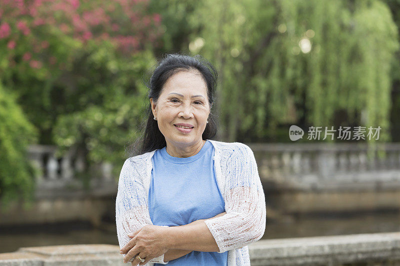 一位年长的亚洲女性双臂交叉站在公园里