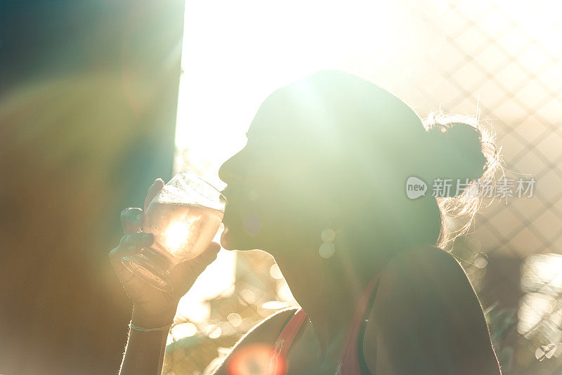 女人的剪影喝啤酒在夏天的太阳背光