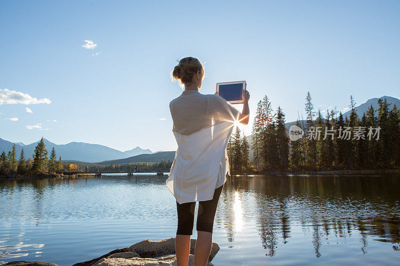 日出时分，一名女子在湖边使用平板电脑