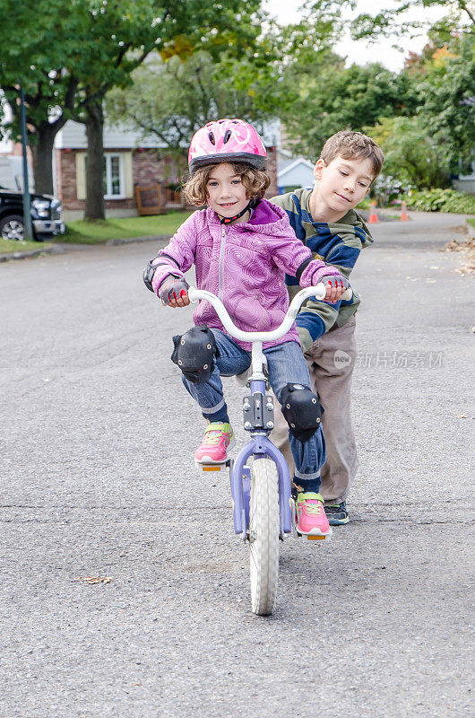 小男孩帮他妹妹骑自行车