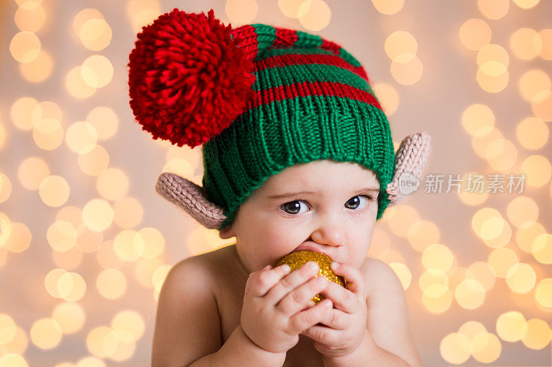可爱的婴儿戴着精灵一样的帽子咬圣诞宝珠