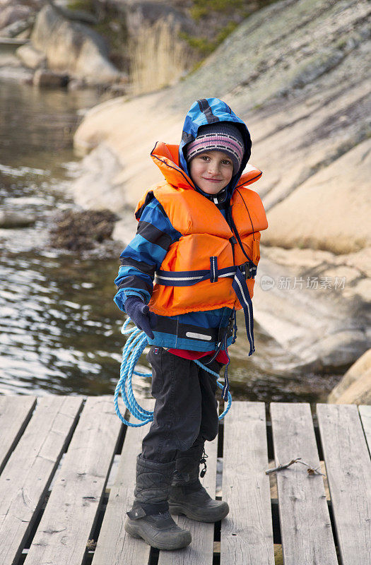 小男孩穿着救生衣和救生绳在水里。