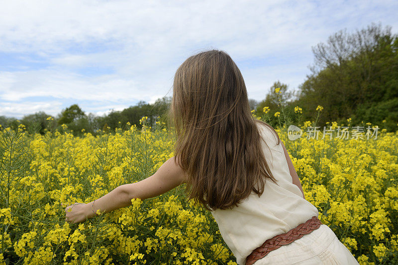 一个少女站在油菜籽地里，摘花