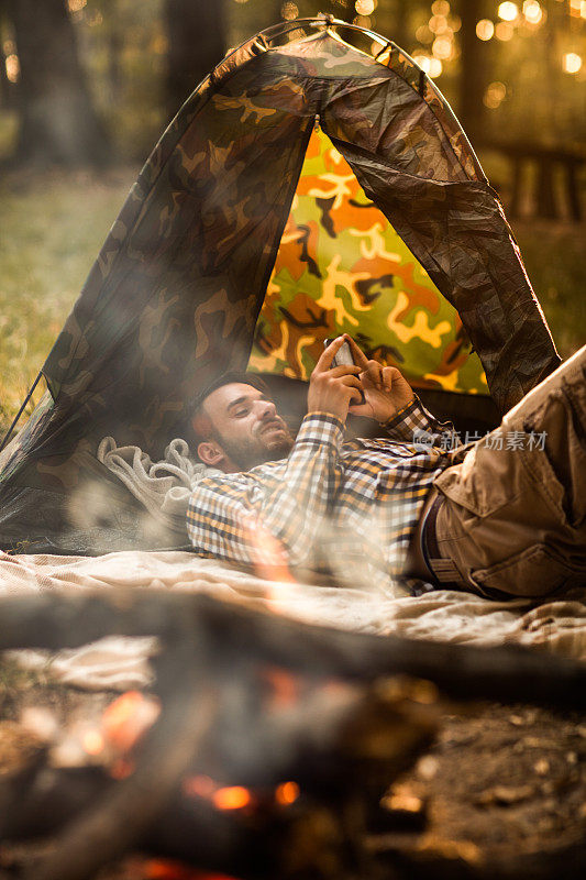 微笑的男人使用手机而放松露营。