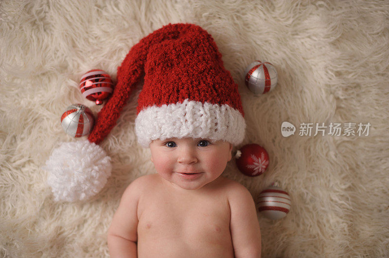 微笑的婴儿戴着圣诞帽，躺在圣诞饰品