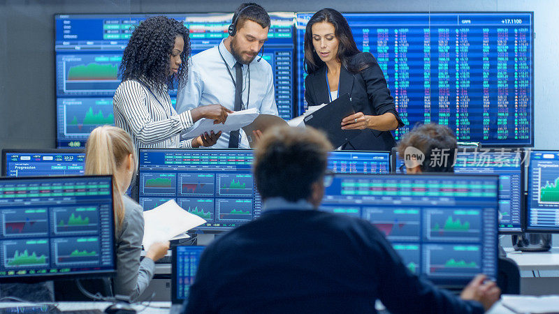 多民族交易员团队在证券交易所办公室忙碌工作。交易商和经纪人在市场上买卖股票。显示器显示相关的信息图，数据和数字。