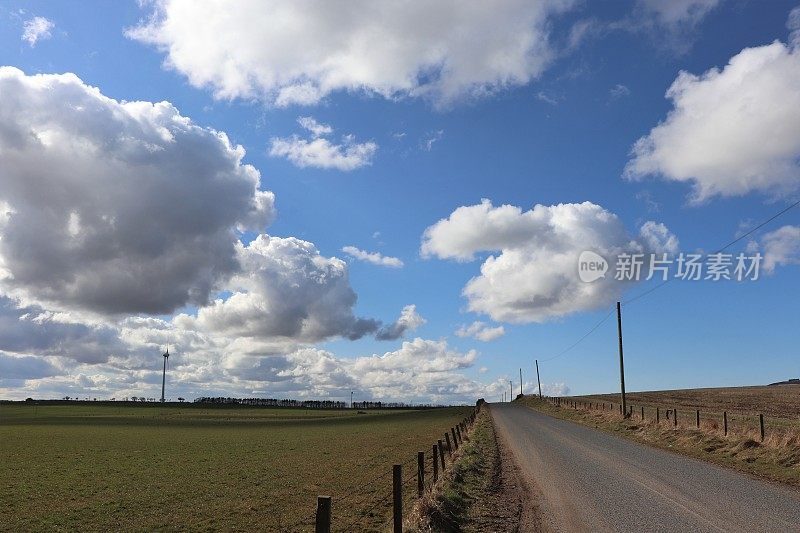 在乡村环境中，蓝天映衬着蓬松的白云，还有风力涡轮机或乡村公路