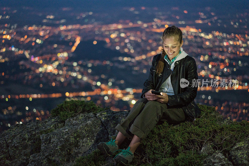 美丽的女人坐在山顶上浏览她的手机。