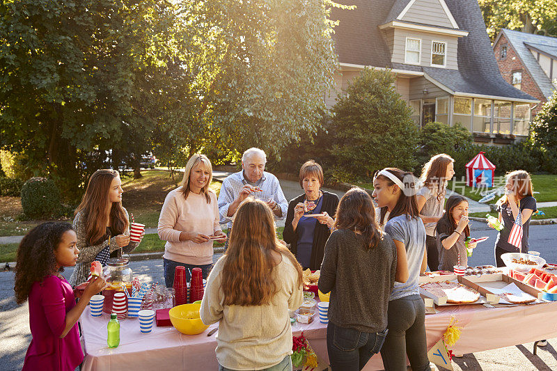 在街区聚会上，邻居们围坐在桌子旁聊天吃饭