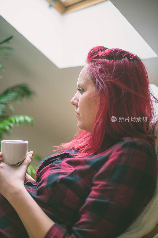 迷人的红发女人坐在椅子上喝咖啡。年轻女孩与热能量饮料。平静和安逸。