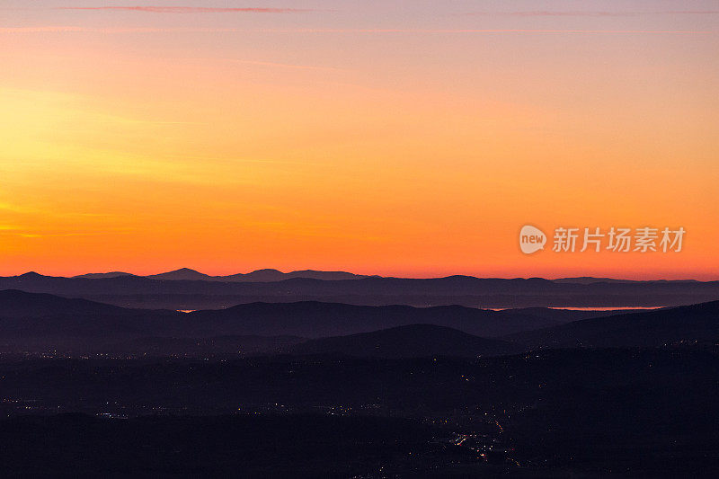 美丽的翁布里亚(意大利)山谷在黄昏的鸟瞰图，山丘，城市灯光和trasiimeno湖反射橙色的天空光