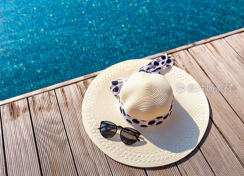 在游泳池的露台上戴着草帽和太阳镜