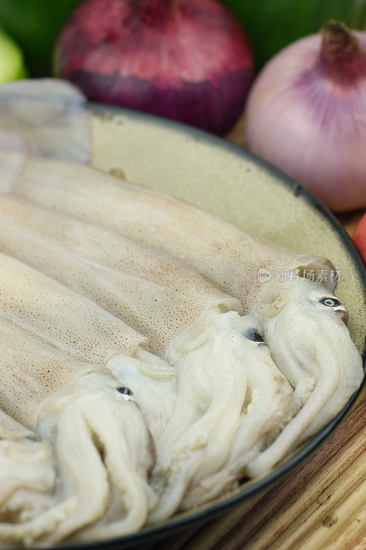 烹饪新鲜的鱿鱼。生墨鱼放在砧板上，前面放青椒，洋葱，西红柿