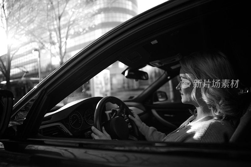 黑白照片的年轻女子驾驶汽车通过城市。