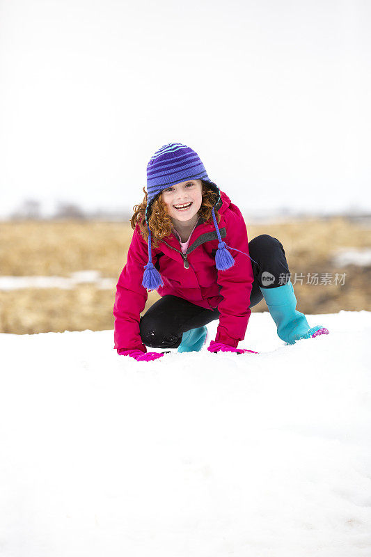 小女孩在雪地里蹲着，对着镜头微笑